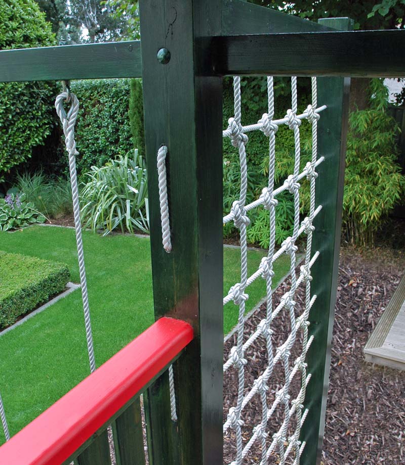 The bespoke wooden climbing frame projects from between the tower and swing set